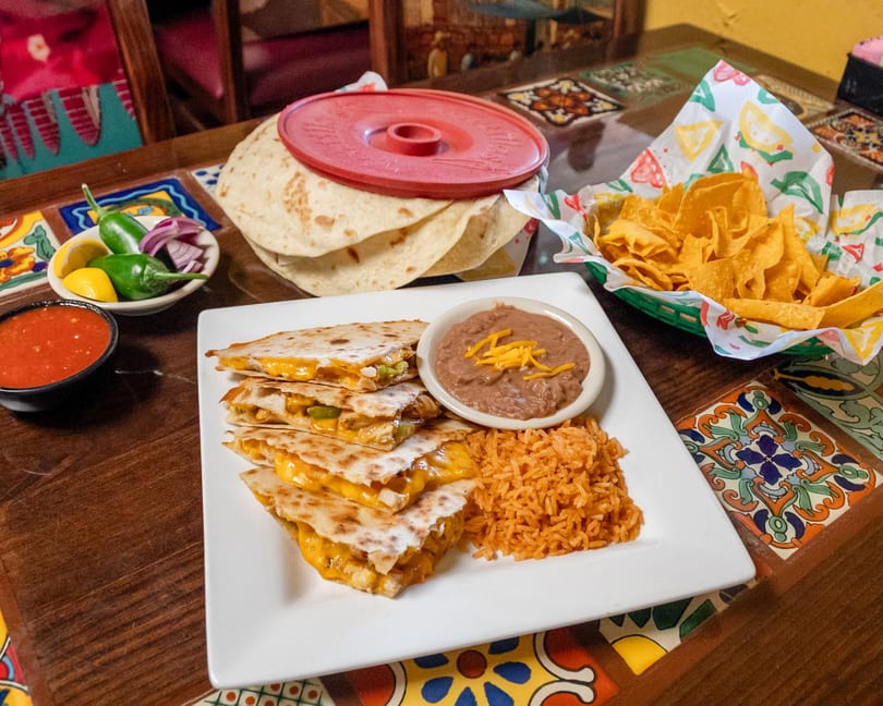Cheesy quesadillas with rice, refried beans, tortilla chips, salsa, and fresh toppings on a vibrant table.